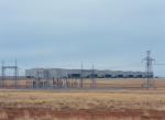 Edifício industrial sem janelas de um data center em paisagem seca, com subestação elétrica e linhas de transmissão em primeiro plano, sob luz difusa. Imagem ilustrativa.